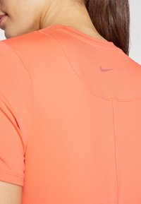 Korte ermer, korallfarget treningsshirt i glatt og stretchy stoff med en liten, lilla Nike-logo nær halsen.