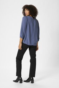 Blusa leggera blu con maniche a sbuffo e vestibilità rilassata. Abbinata a pantaloni neri slim e stivaletti neri lucidi. Design semplice.