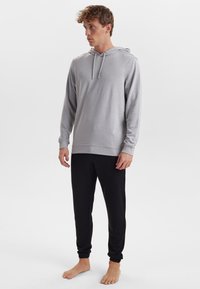 Grå langærmet hættebluse med snoretræk og ribbet kant, sammen med sorte tapered joggers med elastiske manchetter, båret barefoot.