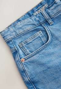 Lichtblauwe spijkerbroek van denim met een vervaagde textuur, met een enkele patch pocket en koperen klinknageldetails op de voorste tailleband.