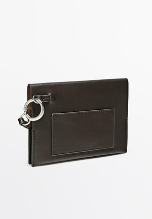 Sort læderpung med en glat tekstur, med en sølvfarvet metalring og en kortplads på forsiden. Rektangulær form.