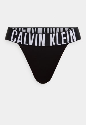 Mustad tangatüüpi aluspesu laiast elastse vöökohaga, millel on suur valge tekst "CALVIN KLEIN".