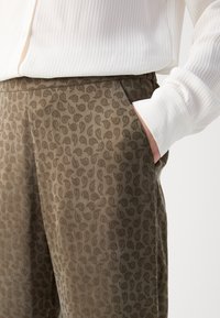 Bruine gestreepte broek met een paisley ontwerp, voorzien van zijzakken en een soepele textuur, gecombineerd met een witte textuurtop.