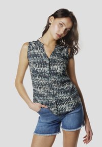 Camisa sin mangas con estampado azul y blanco y cierre de botones en el frente. Combinada con pantalones cortos de mezclilla con bordes deshilachados.