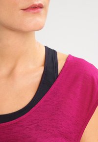 Fuchsiový sportovní top s krátkými rukávy, kulatým výstřihem a texturovaným povrchem, nošený přes černé tílko.