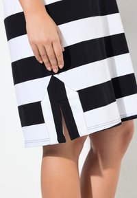Schwarz-weiß gestreiftes Kleid mit einem Schlitz am Saum. Der Stoff wirkt weich; die Streifen sind gleichmäßig verteilt und mit kontrastierenden Nähten versehen.