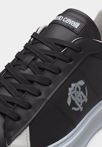 Μαύρο δερμάτινο αθλητικό παπούτσι με μαύρα κορδόνια, λευκή σόλα, λογότυπο φιδιού στο πλάι και τη λέξη "roberto cavalli" στη γλώσσα.