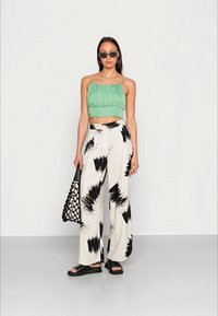 Top verde cropped com textura em ruffles, calças largas com padrão preto e branco, sandálias pretas e uma bolsa tote preta com um design em rede.