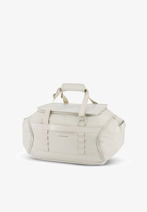 Kermavärinen duffel-laukku, joka on valmistettu kestävästä kankaasta, varustettu vetoketjulla avautuvalla päällä, tukevilla kahvoilla ja säädettävillä hihnoilla, joissa on sileä pinta.