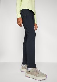 Marineblauwe broek met een slim fit, voorzien van een ritszak op de linker dij, gecombineerd met beige en paarse sportschoenen.