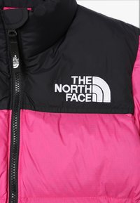 Puchowa kurtka z czarną górną częścią i jasnoróżową dolną częścią. Zamek błyskawiczny i haftowane logo na klatce piersiowej. Gładka faktura.