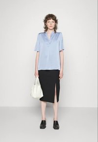 Blusa de satin azul claro com mangas curtas, combinada com uma saia lápis preta com uma fenda lateral. Uma bolsa branca e tamancos pretos completam o visual.