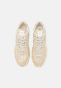 Beige joggesko med perforert skinn og semsket overdel, flate lisser, polstret krage og en subtil logo-lapp på tungen. Gummis�åle.