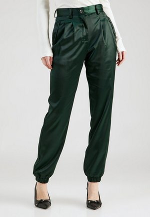 Dark green satin high-waist pants with pleats, elastic cuff hems, paired with black pointed-toe heels and a white ribbed long-sleeve top.