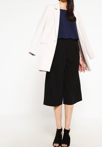 Ljusbeige oversized kavaj, marinblå topp, svarta culottes och svarta öppna klackar; slät tyg, avslappnad passform, elegant design.