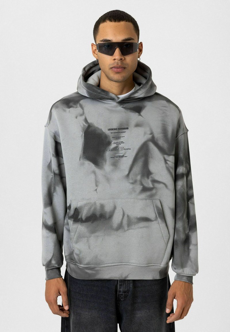 Grijze tie-dye hoodie met een voorzak, voorzien van een bedrukt logo en tekst. De stof lijkt soepel met een comfortabele fit en een grote capuchon.