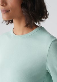 Mintgroene sweatshirt met ronde hals en een gladde textuur, aansluitende mouwen en subtiele stikseldetails. Eenvoudig, casual ontwerp.