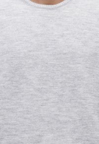 Primo piano di una persona che indossa un maglione a maglia grigio chiaro tinta unita con scollo rotondo e texture morbida.