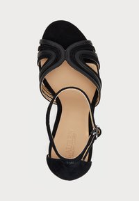 Μαύρη σουέτ πέδιλη γόβα με καμπυλωτές λουρίδες, ανοικτή μύτη και πόρπη στον αστράγαλο. Η λεία δερμάτινη σόλα διαθέτει ανάγλυφο λογότυπο.