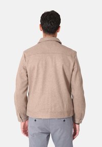 Giacca in misto lana marrone chiaro con collo a rivoltino, cuciture visibili e tasche laterali. Vestibilità ampia e maniche con risvolto.