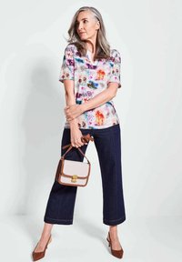 Kleurvol shirt met korte mouwen met bloemmotieven, gecombineerd met donkere wijde jeans. Bruine handtas met een gouden sluiting en bruin hakken.