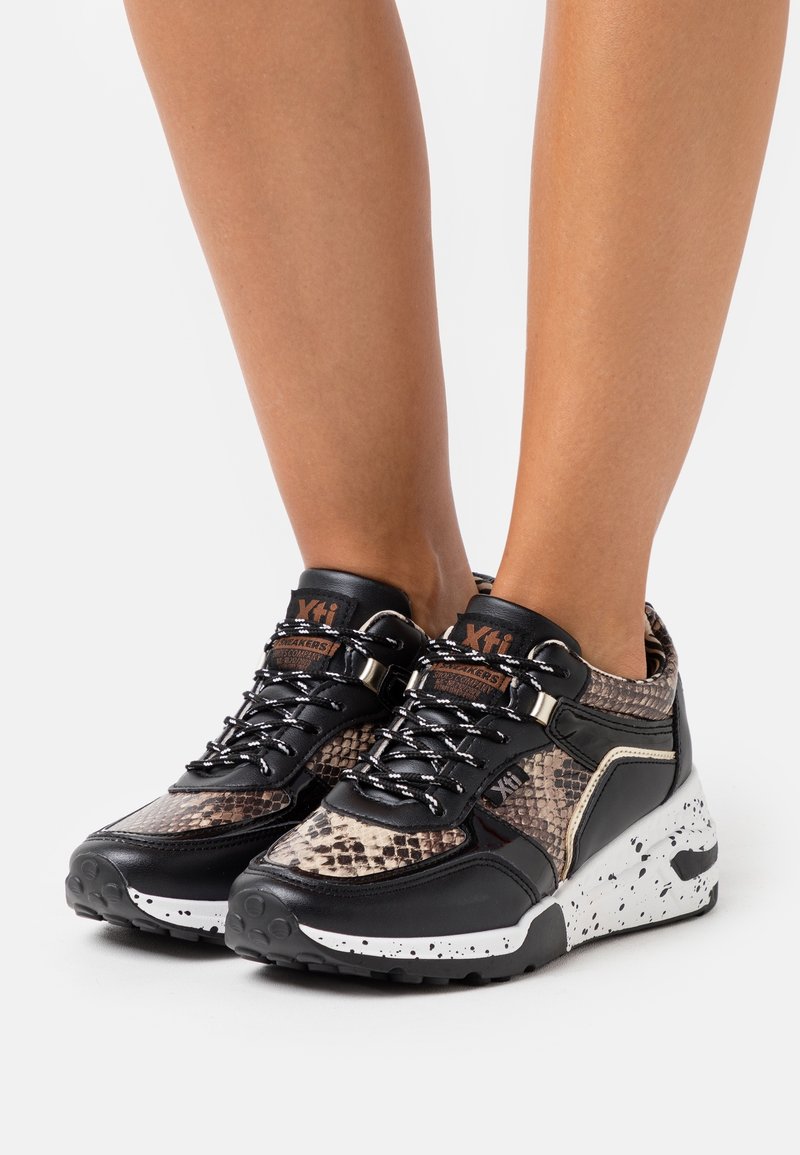 Sporty sneakers with a snakeskin pattern in beige and black, featuring a black leather upper, textured laces, and a speckled white sole.
