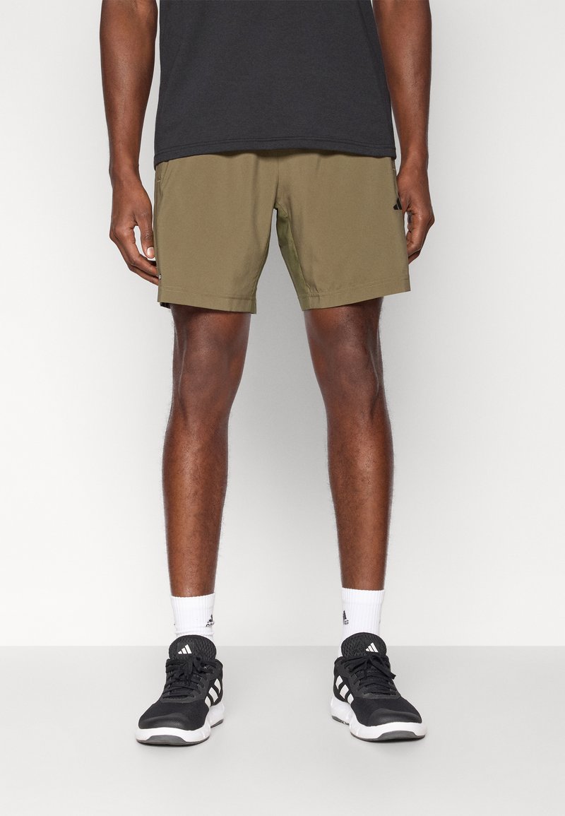 Shorts de sport vert olive à texture lisse, avec poches latérales et coupe droite ; assortis à des chaussures de sport noires et des chaussettes blanches.