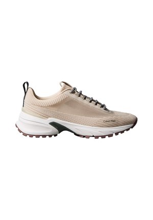 Beżowy dziergany sportowy sneaker z białą grubą podeszwą, czarną pętelką do ściągania, wzorzystymi sznurówkami i logo „Calvin Klein” po boku.
