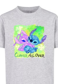 Grå t-shirt med et farverigt grafisk motiv af to tegneseriefigurer, en lilla og en blå, med teksten "CLOVER ALL OVER" i grøn og brun.