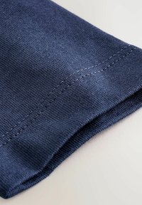 Dunkelblauster Stoff mit glatter Textur, der einen ordentlich genähten Saum und eine leichte Welle am Rand aufweist. Weiches, baumwollähnliches Material sichtbar.