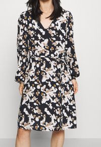 Černé šaty s abstraktním květinovým vzorem v bílé a hnědé barvě, výstřihem do V, dlouhými rukávy, opaskem v pase a splývavým střihem.