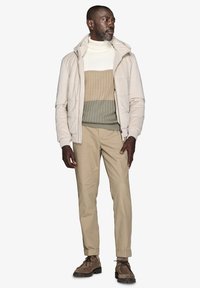 Lys polstret jakke i beige, ribstrikket rullekrave i creme, tan og oliven. Beige chinos, brune snørebåndssko med robuste såler.