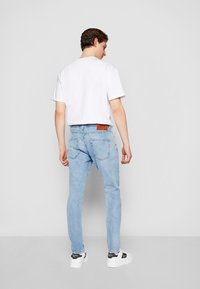 Svetlo modri jeans s slim fit krojem, z rjavim usnjenim logotipom na hrbtu; kombiniran s enostavno belo majico in črnimi spremljevalnimi čevlji.