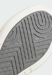 Sole of a sneaker with a grey rubber grip pattern, outlined by a white textured border, featuring curved and zigzag designs for traction.