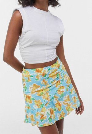 Person iført en hvid ærmeløs crop top og et lyseblåt blomsterprintet skørt med gule og orange blomster.