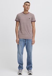 Camiseta de manga corta color burdeos con cuello y dobladillos de las mangas en un tono burdeos contrastante, combinada con jeans azul claro y zapatillas grises.