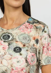 Kortermet topp med blomsterprint i rosa, svart og grønn, rund hals og mykt, teksturert stoff.