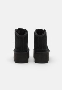 Botine negre din suede, cu vârful rotund, având o talpă groasă și căptușeală moale și pufoasă la gât.