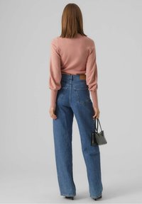 Maglione rosa a coste con maniche a sbuffo abbinato a jeans blu a vita alta e dalla vestibilità comoda. Una borsa nera completa il look.