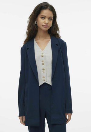 Blazer taillé bleu marine sur un gilet gris clair à boutons. Le blazer présente un col cranté et des manches longues, créant une silhouette structurée.