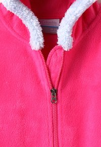 Fleecová bunda v jasně růžové barvě se zapínáním na zip. Má měkkou, bílou, nadýchanou podšívku kolem kapuce a oblasti krku.