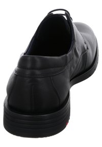 Schwarzer Lederschuh mit glatter Textur, abgerundeter Ferse und gepolstertem Kragen. Verfügt über eine Gummisohle mit horizontalen Rillen und roten Akzenten.