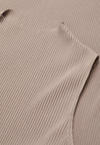 Tejido de ribete beige claro con una textura suave y una forma ajustada. El diseño cuenta con un escote redondeado y sutiles detalles de costura.