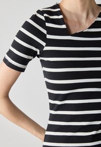 Black and white striped T-shirt with a rounded neckline, short sleeves, and soft, fitted fabric. Horizontal stripes alternate in width.