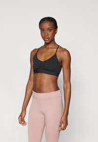 Μαύρο αθλητικό μπουστάκι με λεπτές τιράντες και συγκέντρωση στο κέντρο, σε συνδυασμό με ανοιχτό ροζ ψηλόμεσο κολάν, με λεία υφή και απλό σχέδιο.