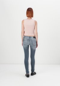 Top corto de canalé en rosa claro con un acabado texturizado, diseño sin mangas, combinado con jeans skinny de tiro medio, de color azul deslavado y zapatos negros.