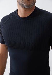 Námořnická modrá sportovní košile s krátkým rukávem, s žebrovanou texturou v horní části a hladkou dolní částí.