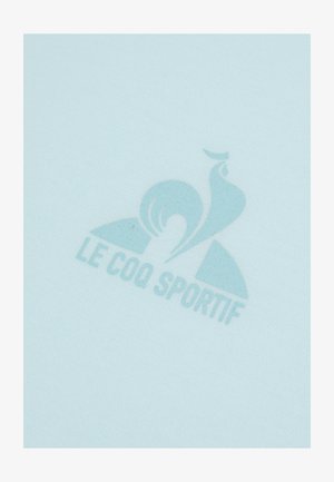 La tela azul claro presenta un sutil logotipo impreso de "Le Coq Sportif", destacando su suave textura y un diseño minimalista.
