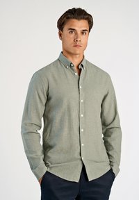 Jasnozielona koszula na guziki z teksturowanej tkaniny, z długimi rękawami i ostrym kołnierzykiem. Na przodzie znajdują się białe guziki.
