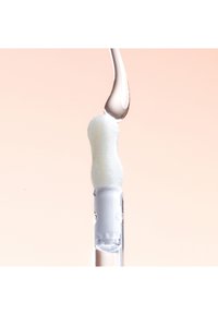Applicateur blanc avec un embout arrondi et texturé, relié à un tube en plastique transparent, avec une goutte de liquide au-dessus. Surfaces douces et lisses.